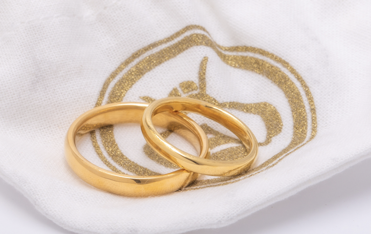   A pair of 24K classic wedding bands, the first pair ever crafted from traceable and responsible mercury-free artisanal gold from the Democratic Republic of Congo, sit atop Reflective Jewelry's drawstring bee bag.